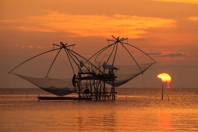 Fishing net in sea against sky during sunset