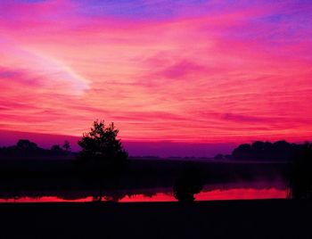 Silhouette trees by lake against romantic sky at sunset