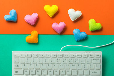 High angle view of keyboard and heart shape decorations on colored background