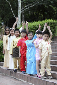 Cute friends with hand raised in traditional clothing standing on steps
