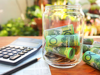 Close-up of paper currency in glass of jar by calculator and paper on table