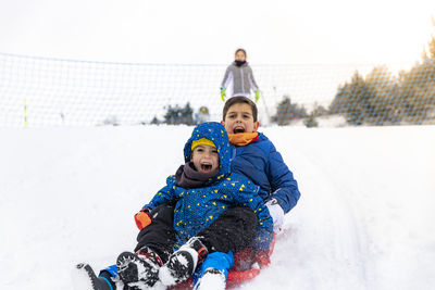 Full length of siblings tobogganing on snow during winter