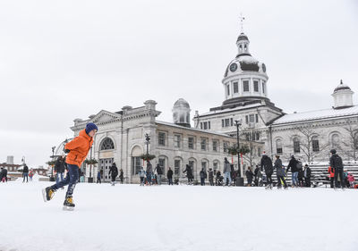 Adolescent boy skating on outdoor ice rink on cloudy day.