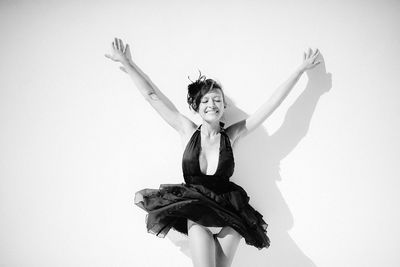 Smiling young woman with eyes closed dancing against white background