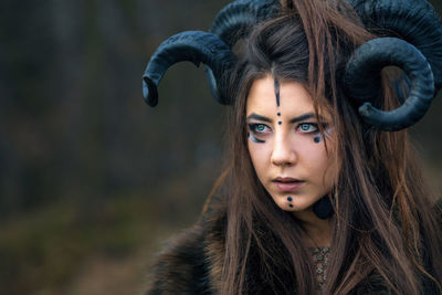 Close-up of serious woman with painted face wearing horns