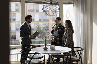 Salesman taking with couple while standing near table during meeting at home