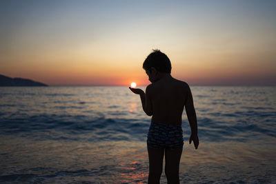 Little kid playing with the sun on the beach at sunset