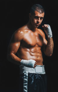 Portrait of shirtless male athlete wearing hand wrap while standing against black background