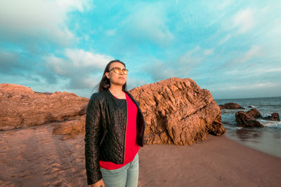 Young man standing on rock by sea against sky