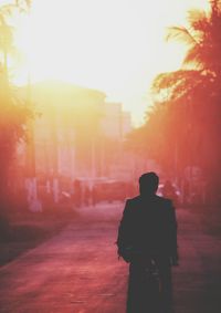 Rear view of silhouette man on road against sky during sunset