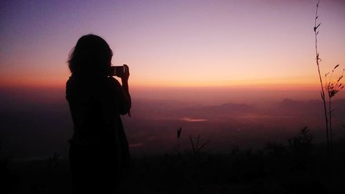 Silhouette woman photographing against sky during sunset