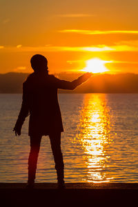 Silhouette man standing on beach against orange sky