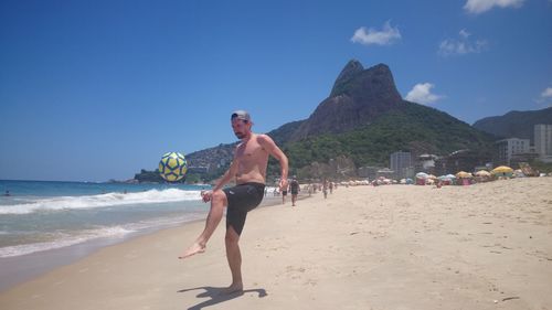 Full length of shirtless man playing with ball at beach against sky