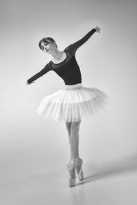 A ballerina in a bodysuit and tutu poses in motion showing ballet elements while standing on pointes