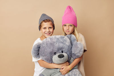 Portrait of sibling with stuffed toy against beige background