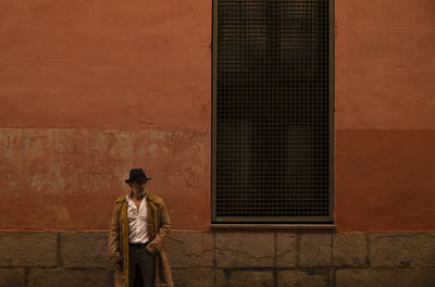 Adult man in hat and coat in front of red wall on street. madrid, spain