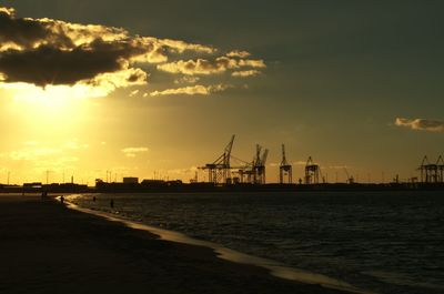 Silhouette of cranes at harbor during sunset