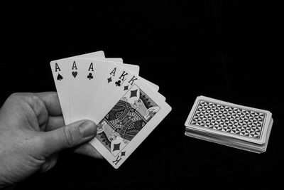 Cropped image of hand holding playing cards over black background