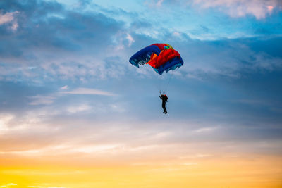 Low angle view of person paragliding against sky during sunset