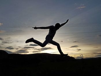 Silhouette of young man jumping over field against sky during sunset