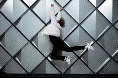 Side view of young woman in mid-air jumping against pattern wall