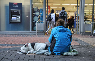 Man and dog sitting on footpath in city