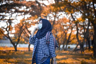 Rear view of woman standing amidst trees during autumn