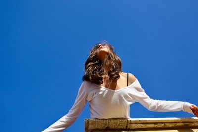 Low angle view of woman against clear blue sky