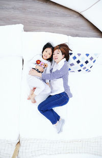 High angle portrait of mother with daughter lying on duvet at home