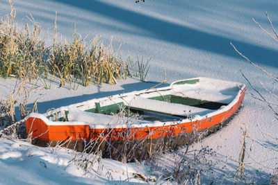 Wooden colorful boat stacked on a frozen lake covered by snow on the beach with reeds