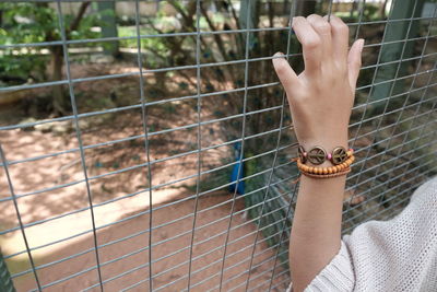 Cropped image of hand touching fence with peacock in background