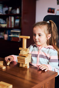 Cute girl playing with wooden blocks on table at home