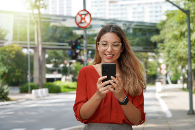 Beautiful smart woman with glasses using mobile phone walking in sao paulo metropolis in brazil