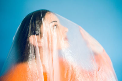 Teenage girl wrapped in plastic against blue background