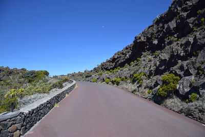 Road by mountain against clear blue sky