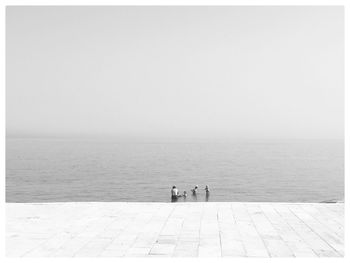 People standing by sea against clear sky