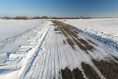 Tire tracks on snow field against sky