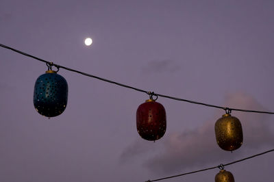 Low angle view of lanterns hanging from cable against sky at dusk