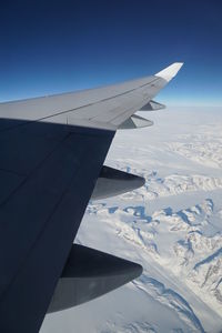 Airplane flying over snowcapped landscape against blue sky