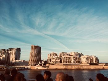 People on city buildings by sea against sky