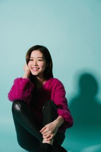 Portrait of smiling young woman sitting against blue background