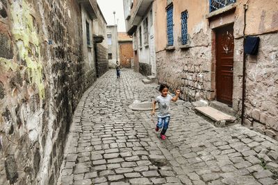 Girl running on footpath amidst buildings in city