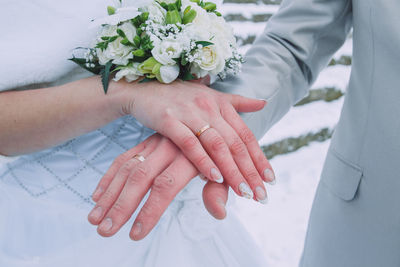 Midsection of groom and bride with bouquet