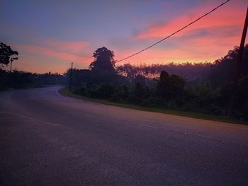 Road by trees against sky during sunset