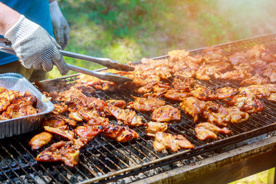 Cropped image of person cooking meat on barbecue grill