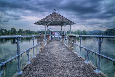 Empty gazebo over river against cloudy sky