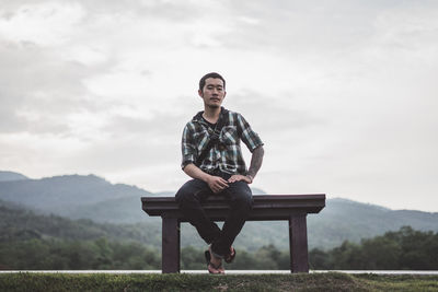 Full length of young man sitting on seat against sky
