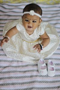 Portrait of cute baby girl sitting on bed at home