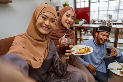 Smiling woman taking selfie while sitting at dining table