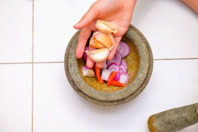 Cropped hand of woman putting garlics in mortar and pestle